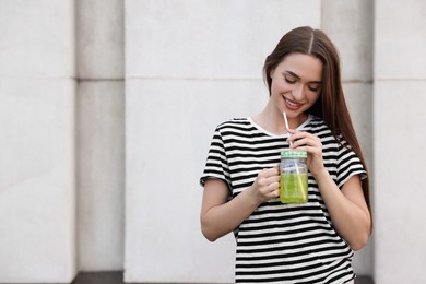 Photo of Young woman with mason jar of fresh juice outdoors, space for text