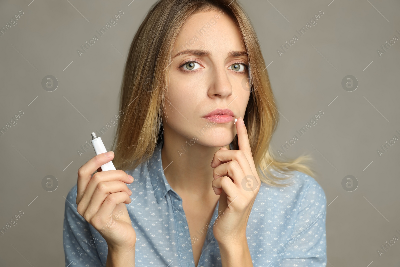 Photo of Woman with herpes applying cream onto lip against  light grey background