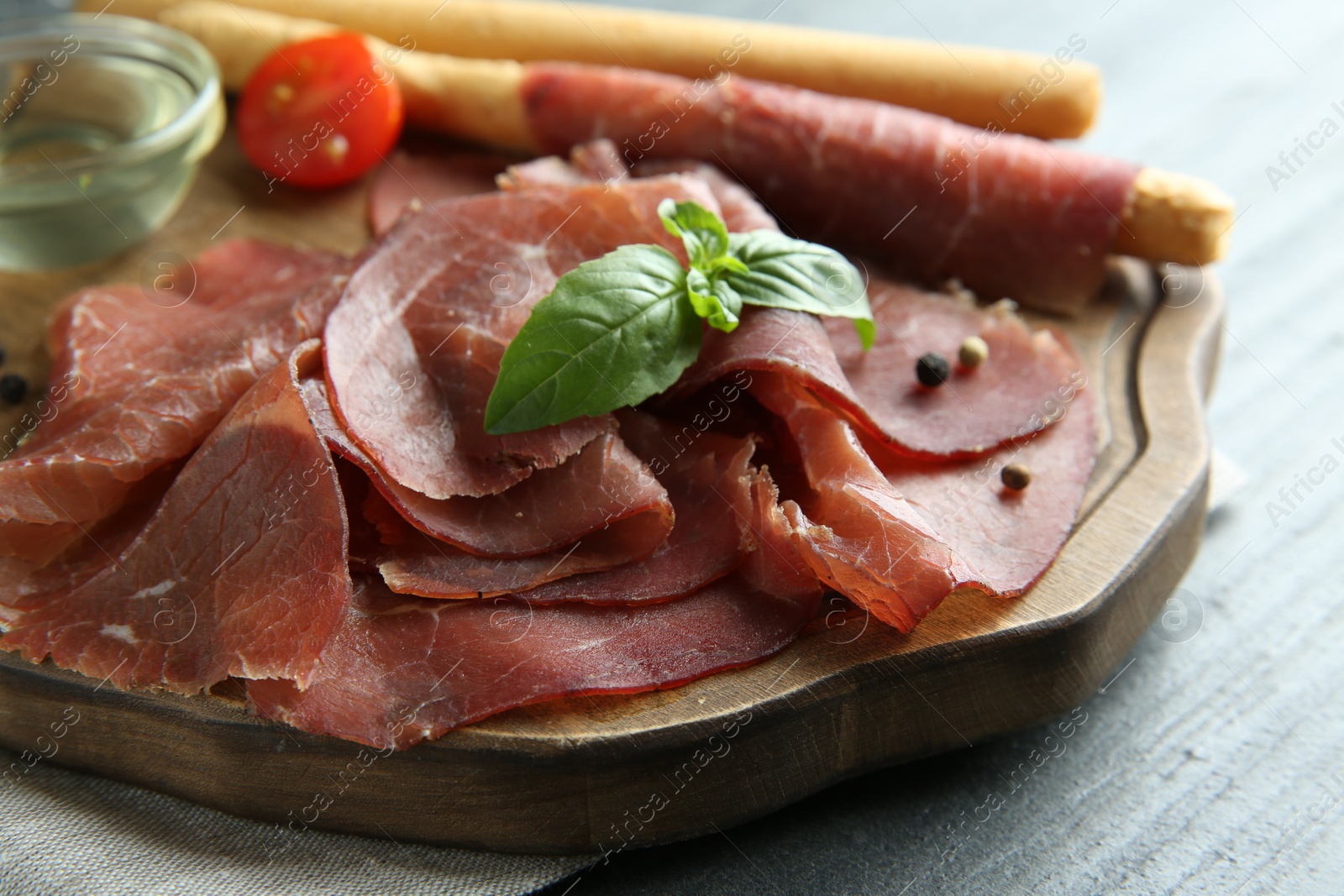 Photo of Delicious bresaola and basil leaves on grey textured table, closeup