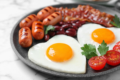 Delicious breakfast with heart shaped fried eggs and  sausages on white marble table, closeup