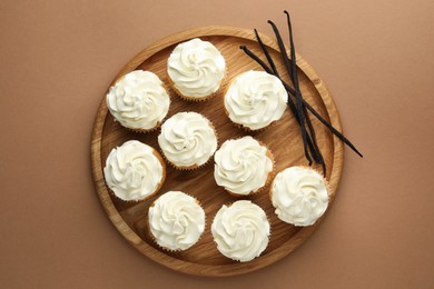 Photo of Tasty cupcakes with cream and vanilla pods on dark beige background, top view