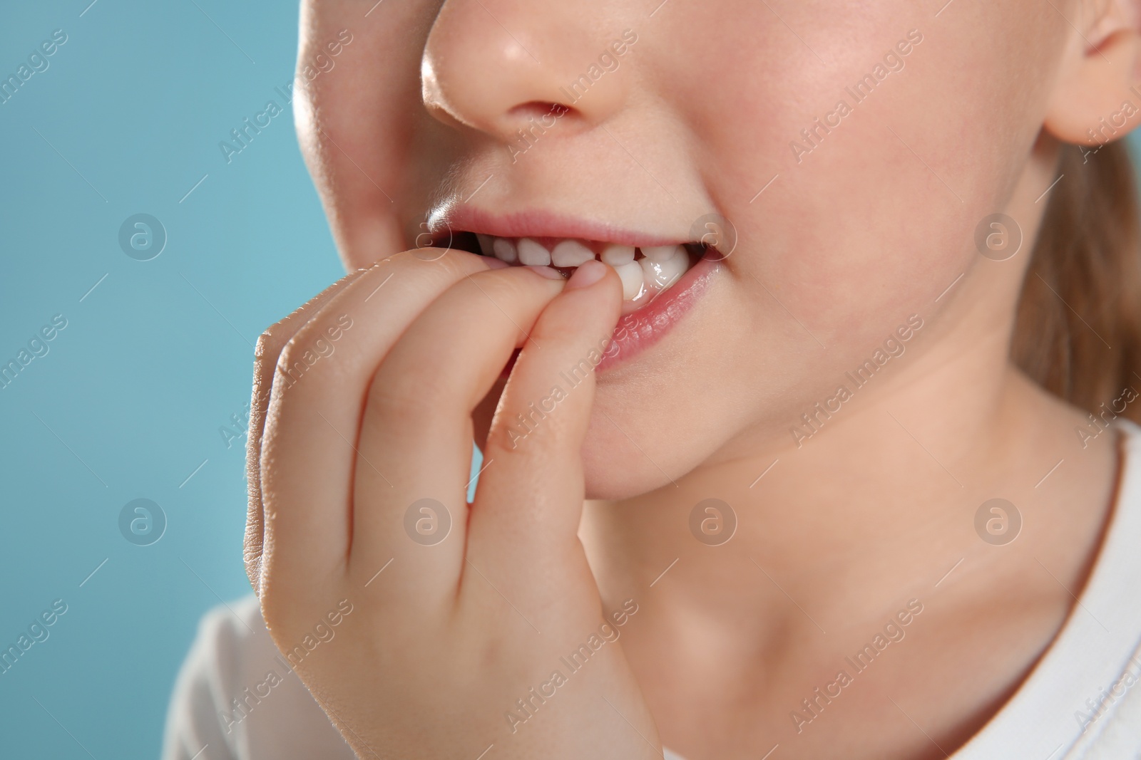 Photo of Little girl biting her nails on turquoise background, closeup