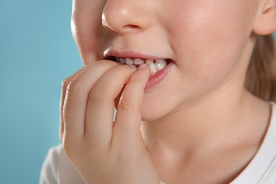 Photo of Little girl biting her nails on turquoise background, closeup