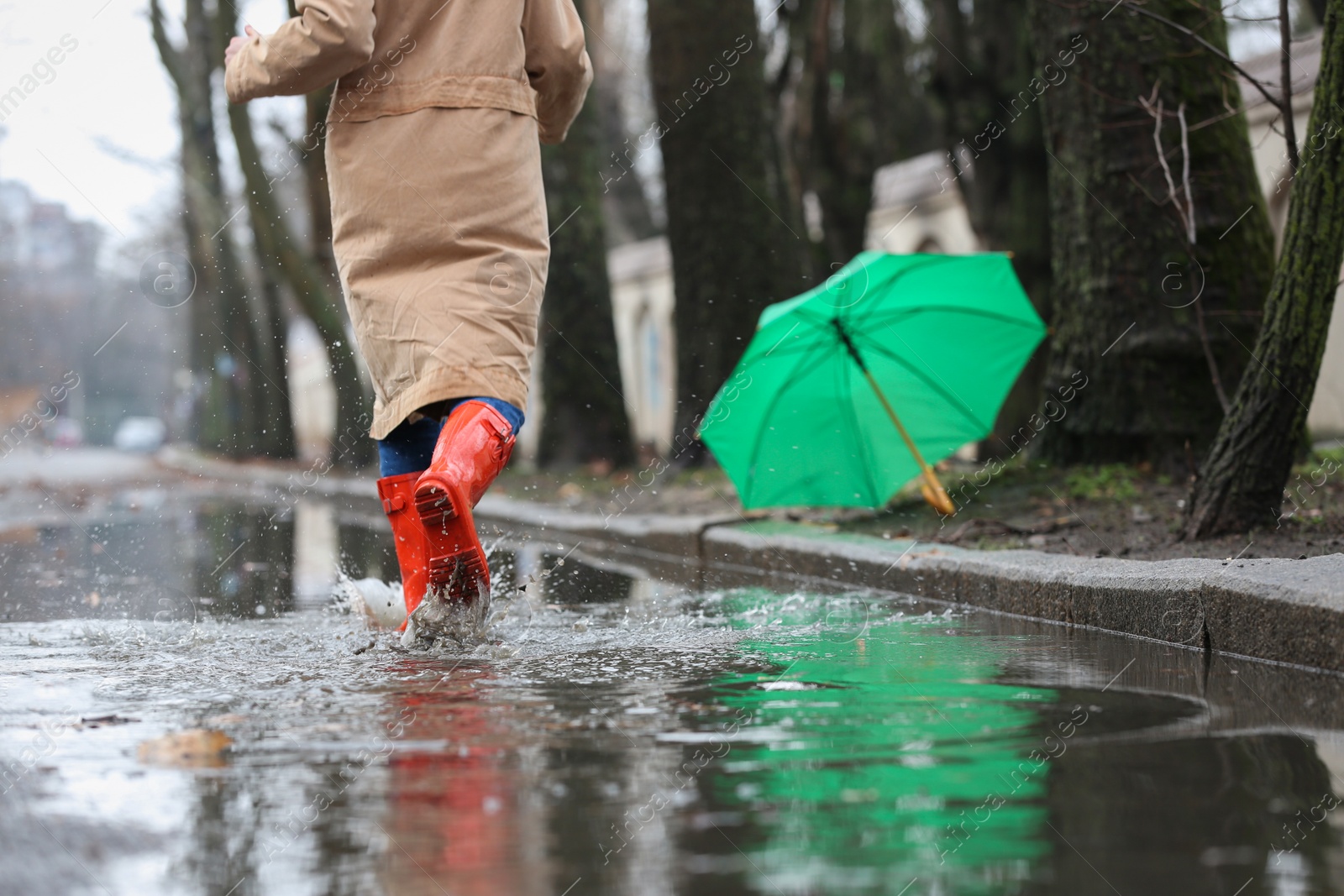 Photo of Woman in rubber boots running after umbrella outdoors on rainy day, closeup