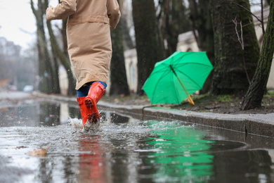 Photo of Woman in rubber boots running after umbrella outdoors on rainy day, closeup