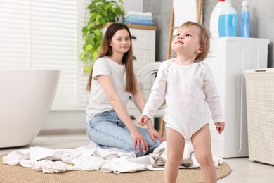 Photo of Little girl, baby clothes and mother in bathroom, selective focus