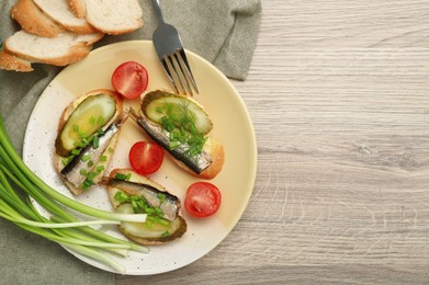 Photo of Delicious sandwiches with sprats, pickled cucumber and green onion served with tomatoes on wooden table, flat lay. Space for text