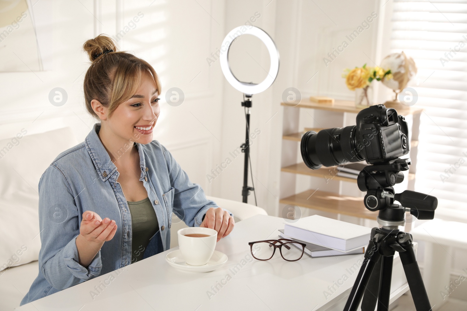 Photo of Blogger with cup of tea recording video at table indoors. Using ring lamp and camera