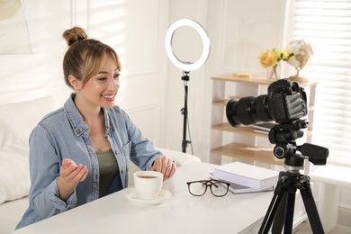 Blogger with cup of tea recording video at table indoors. Using ring lamp and camera
