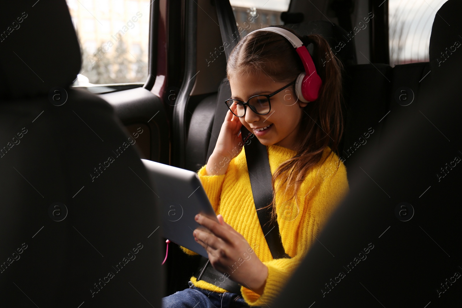 Photo of Cute little girl listening to audiobook in car