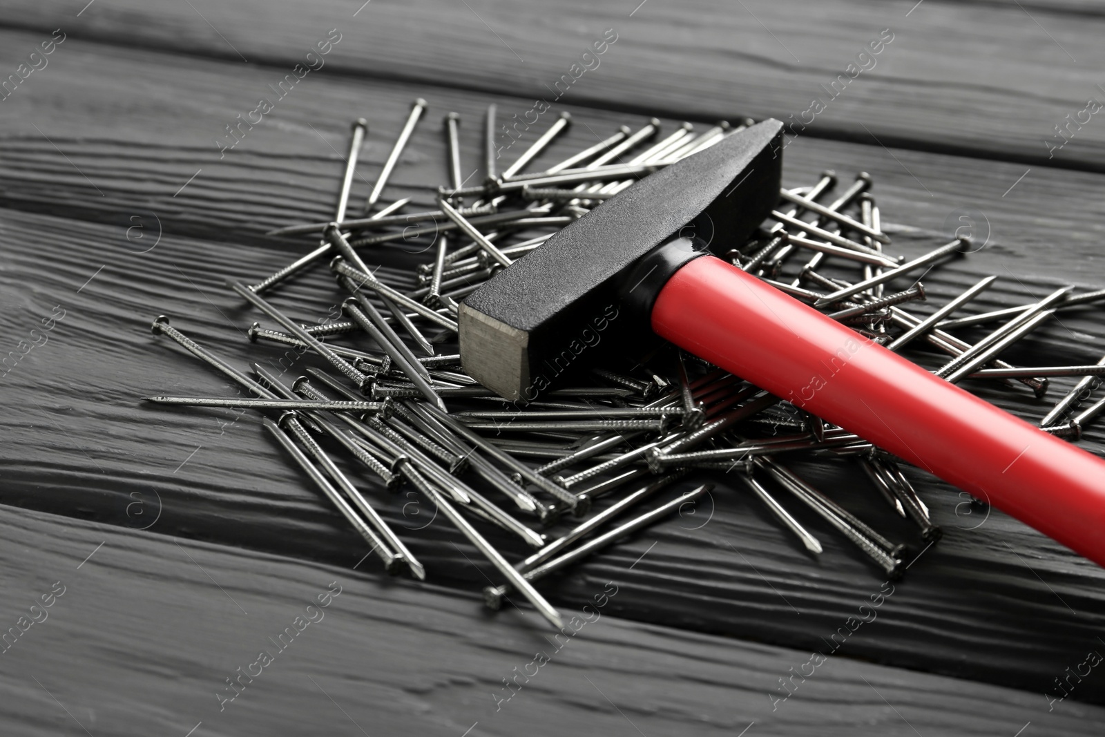 Photo of Hammer and metal nails on black wooden table, closeup