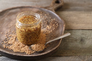 Jar and spoon of whole grain mustard on wooden table. Space for text