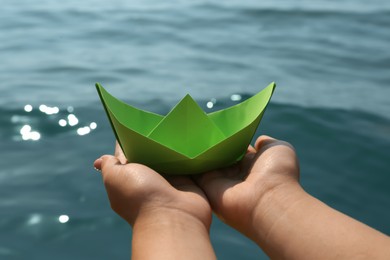 Photo of Woman holding light green paper boat near sea, closeup