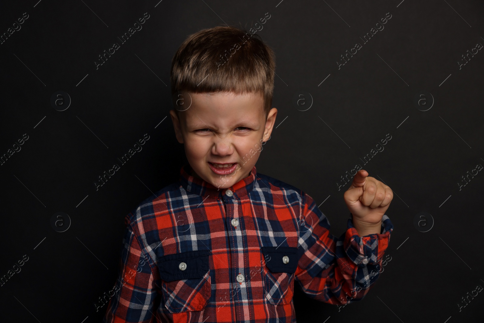 Photo of Angry little boy on black background. Aggressive behavior