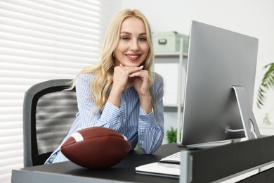 Happy woman with american football ball at table in office