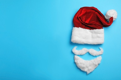 Photo of Santa Claus hat and beard on light blue background, flat lay. Space for text