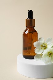 Photo of Bottle of cosmetic oil and flowers on beige background, closeup