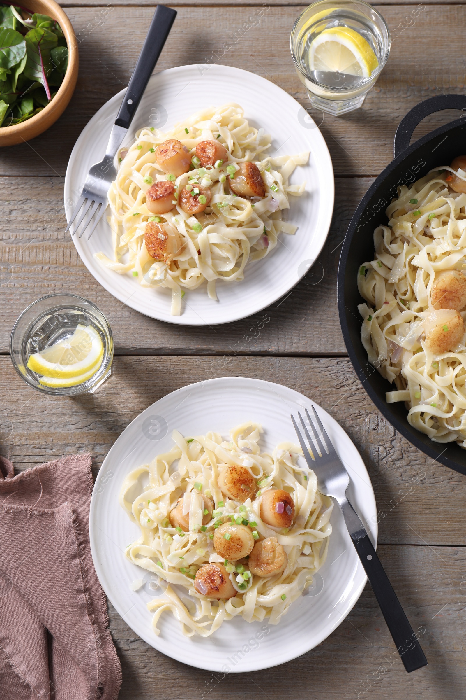 Photo of Delicious scallop pasta with onion served on wooden table, flat lay