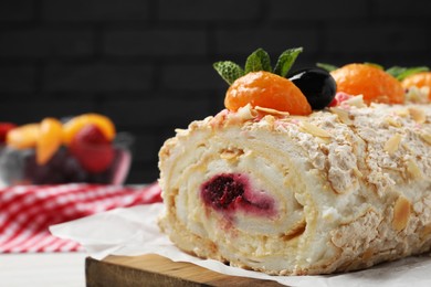 Tasty meringue roll with jam, tangerine slices and mint leaves on wooden board, closeup