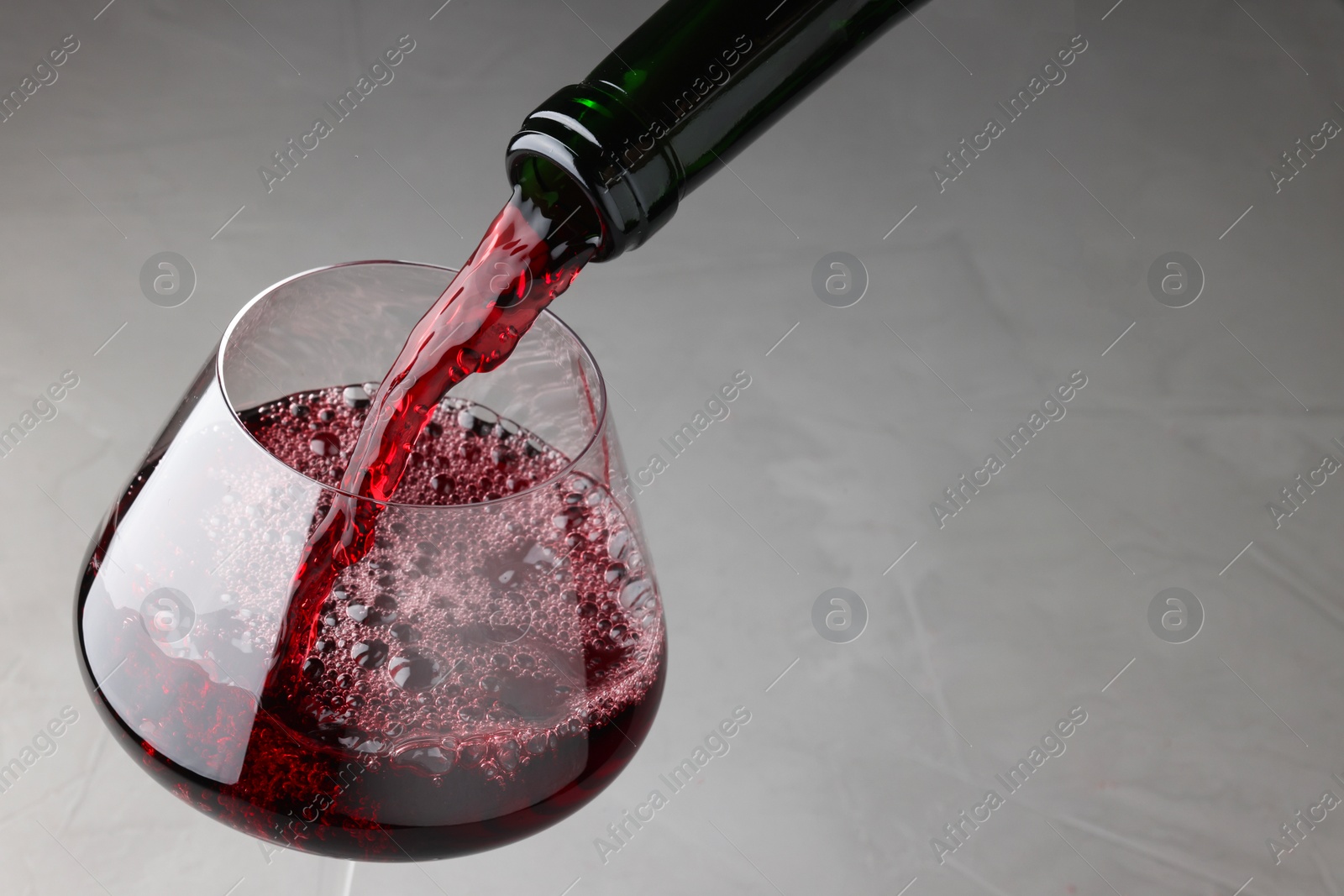 Photo of Pouring tasty red wine in glass at gray table, closeup. Space for text