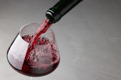 Photo of Pouring tasty red wine in glass at gray table, closeup. Space for text