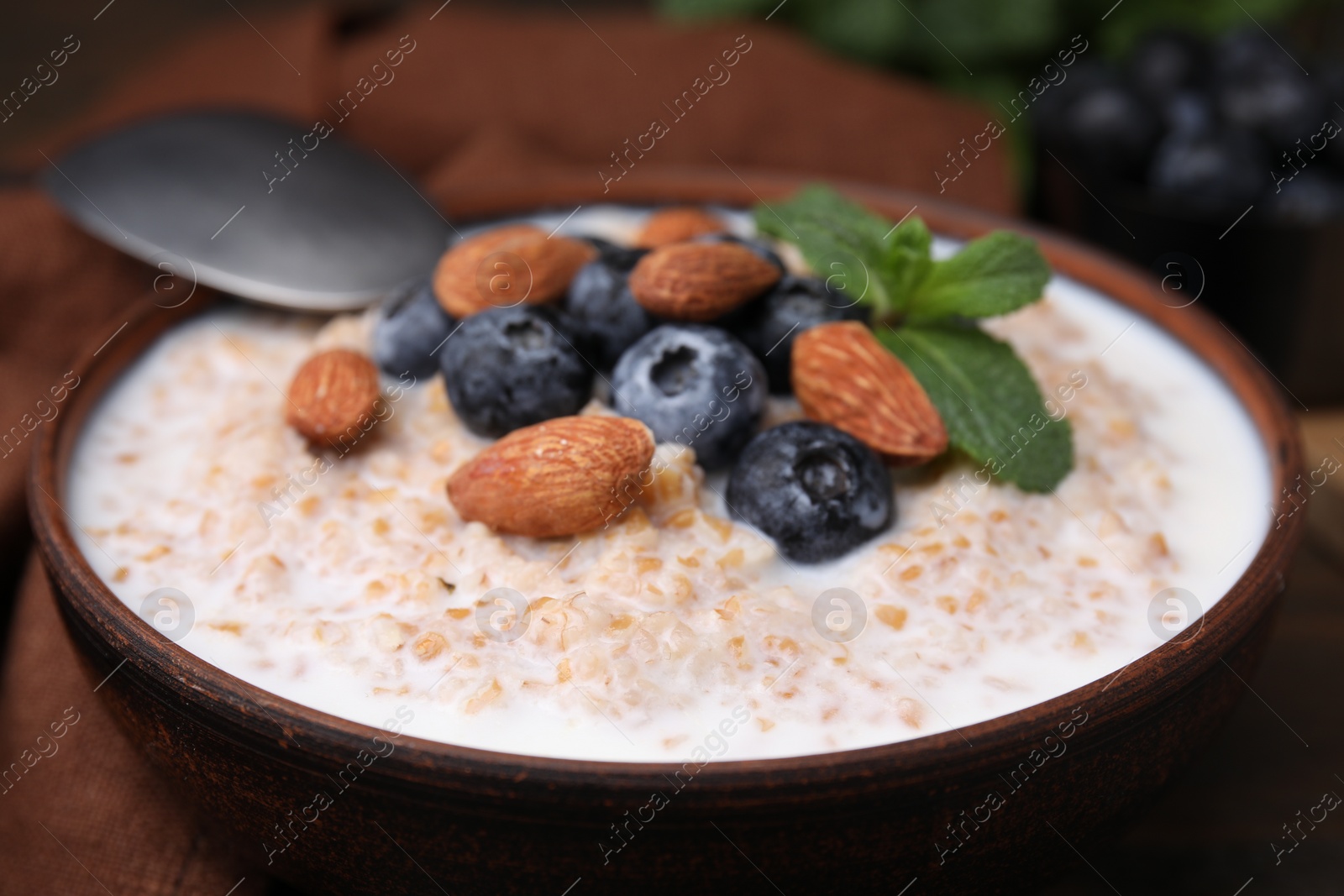 Photo of Tasty wheat porridge with milk, blueberries and almonds in bowl on table, closeup