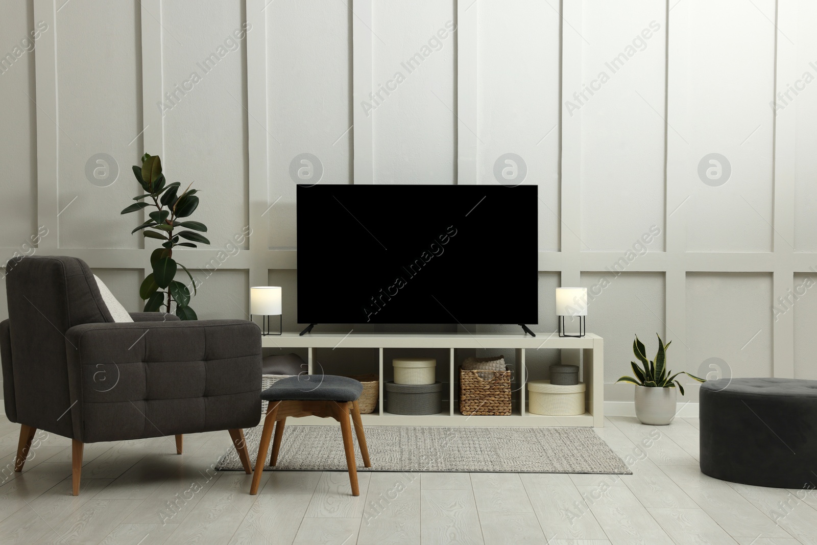 Photo of Modern TV on cabinet, beautiful houseplants and armchair indoors. Interior design
