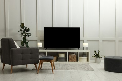 Modern TV on cabinet, beautiful houseplants and armchair indoors. Interior design