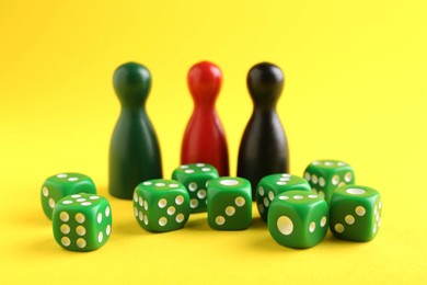 Photo of Many green dices and color game pieces on yellow background, closeup