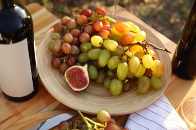 Photo of Red wine and fruits served for picnic on wooden table outdoors