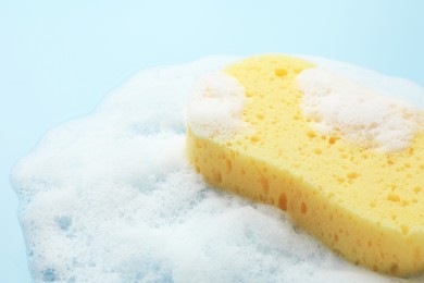 Photo of Yellow sponge with foam on light blue background, closeup