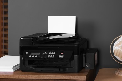 Modern printer with paper on wooden desk at home