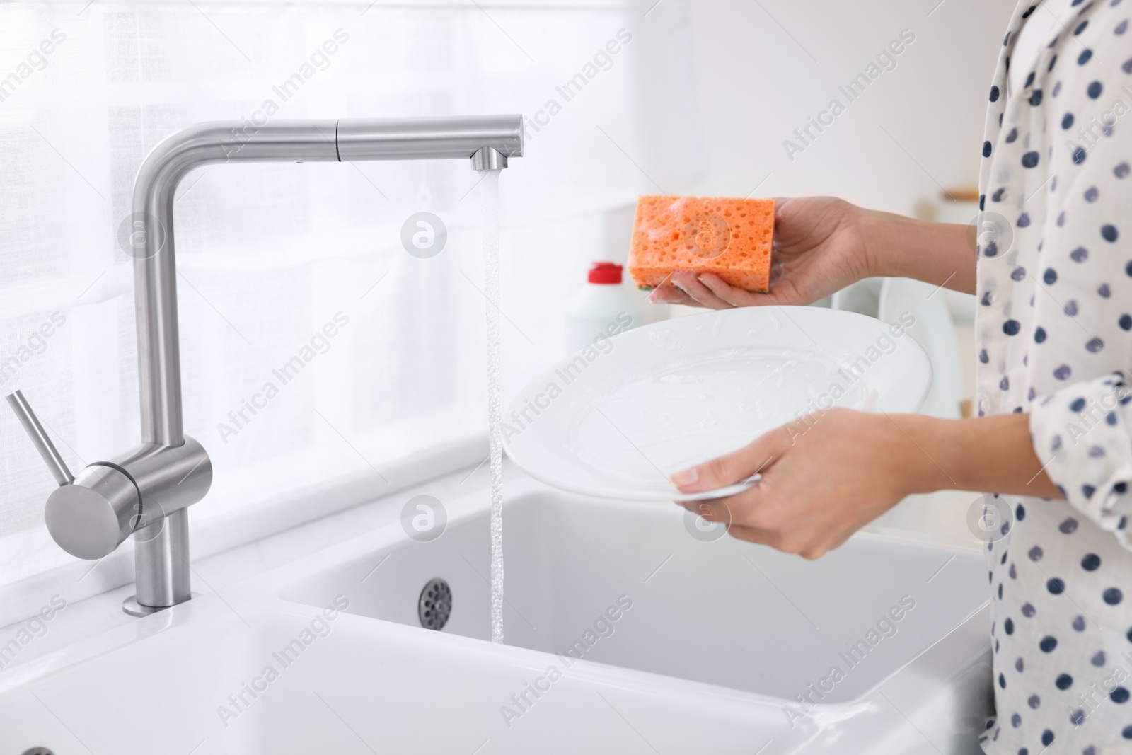 Photo of Woman washing plate above sink in modern kitchen, closeup