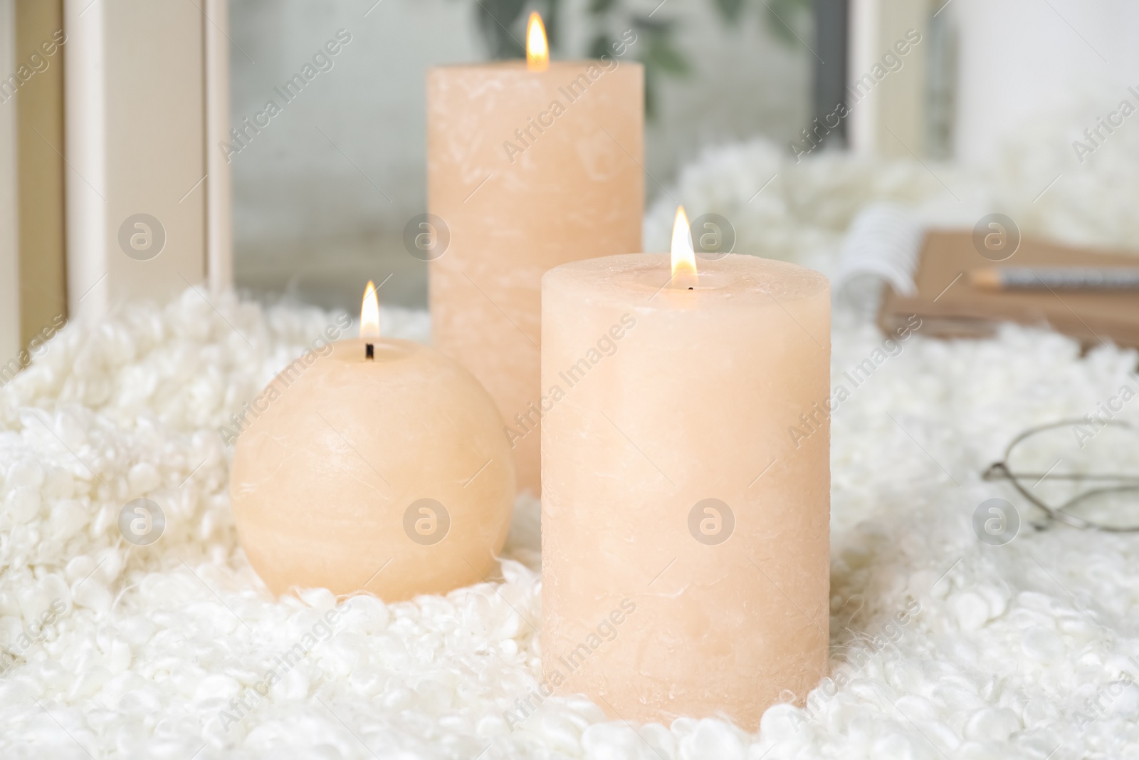 Photo of Burning wax candles on soft fabric indoors