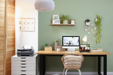 Stylish workplace with computer, laptop and lamp near olive wall at home