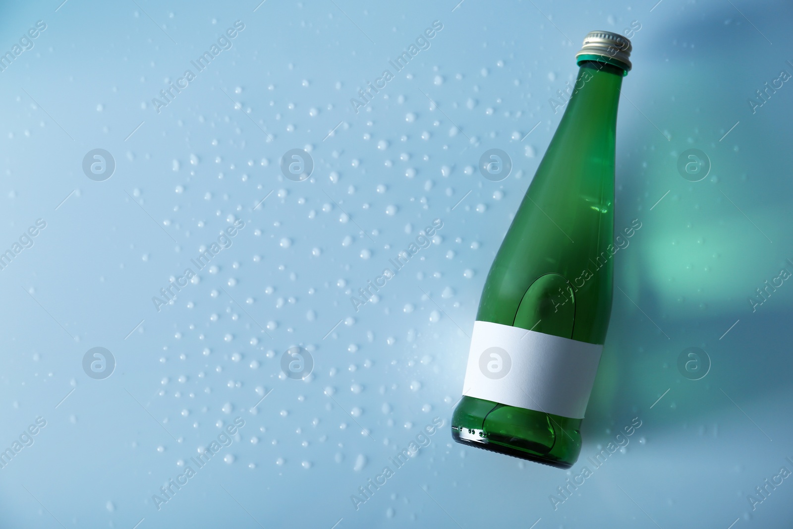 Photo of Bottle of water on wet light surface, top view. Space for text