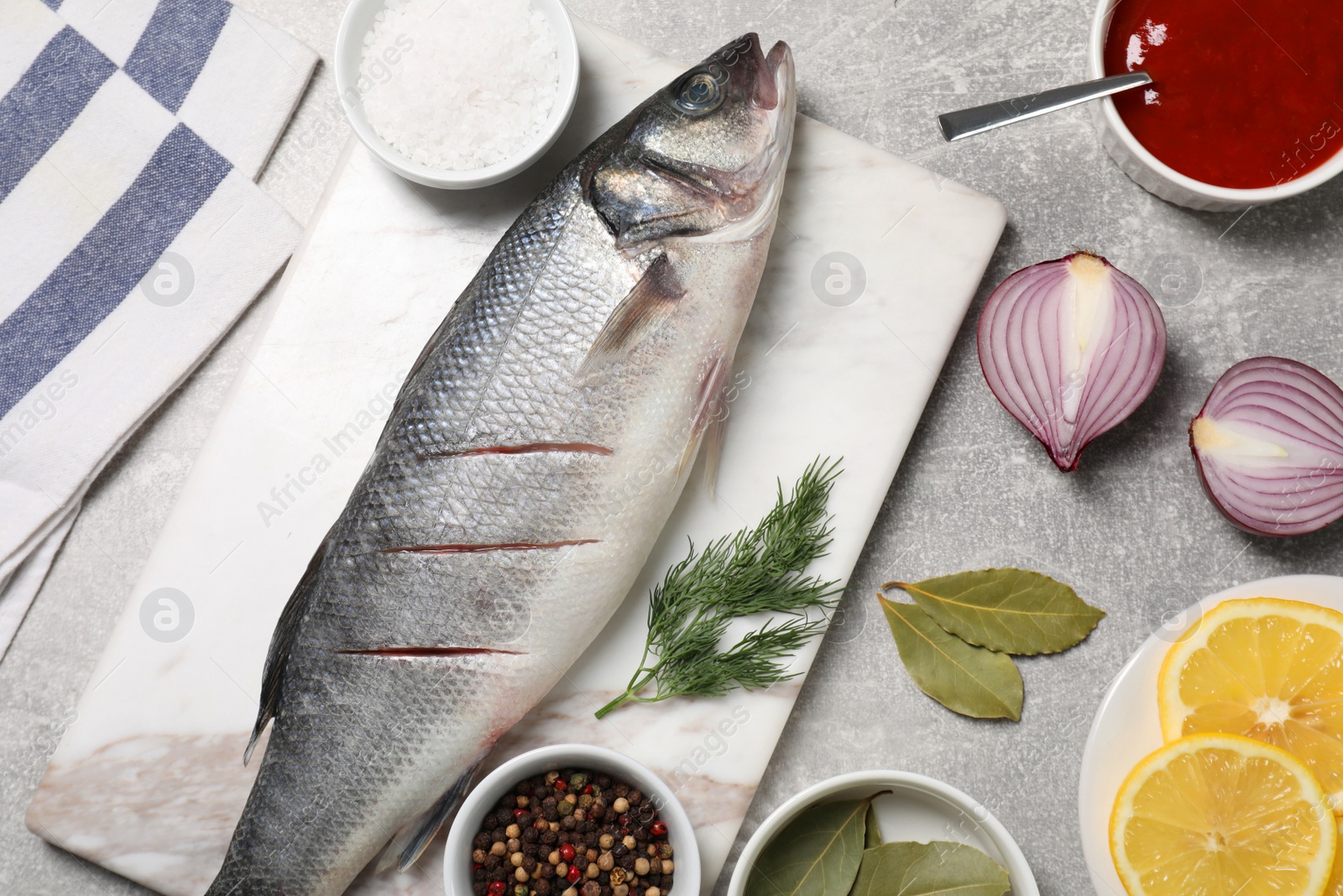 Photo of Fresh raw sea bass fish and ingredients on light gray table, flat lay