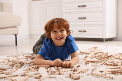 Photo of Cute little boy playing with wooden construction set on carpet at home. Child's toy