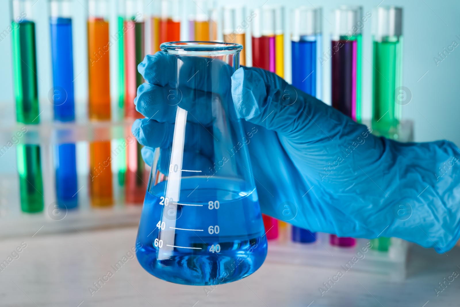 Photo of Scientist holding flask with liquid at wooden table, closeup