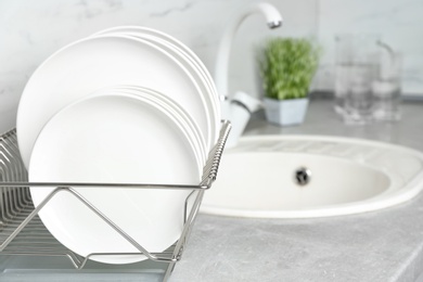 Photo of Different clean plates in dish drying rack on kitchen counter