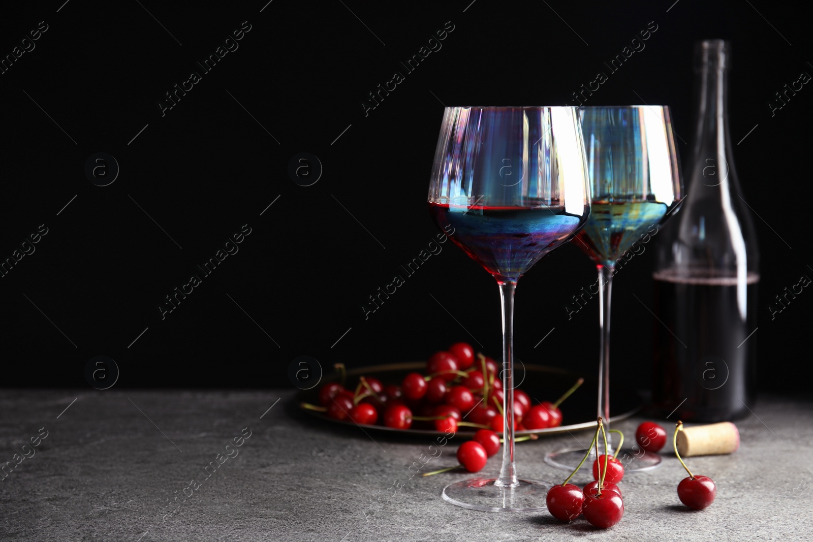 Photo of Delicious cherry wine and ripe juicy berries on grey table against black background. Space for text