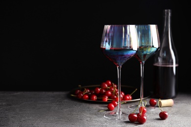 Photo of Delicious cherry wine and ripe juicy berries on grey table against black background. Space for text