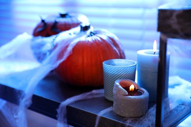 Photo of Candles, pumpkins and fake spiderweb on stand indoors. Halloween decoration