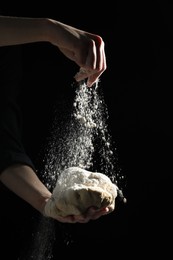 Photo of Making bread. Woman sprinkling flour over dough on dark background, closeup