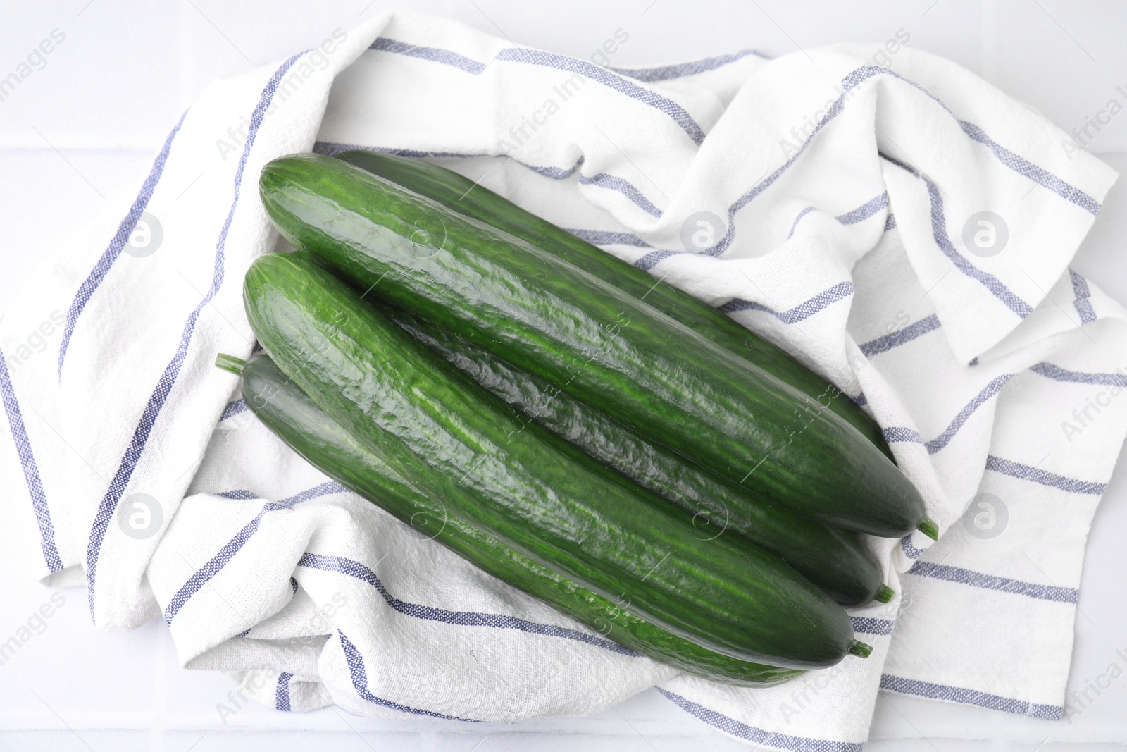 Photo of Fresh cucumbers and cloth on white table, top view