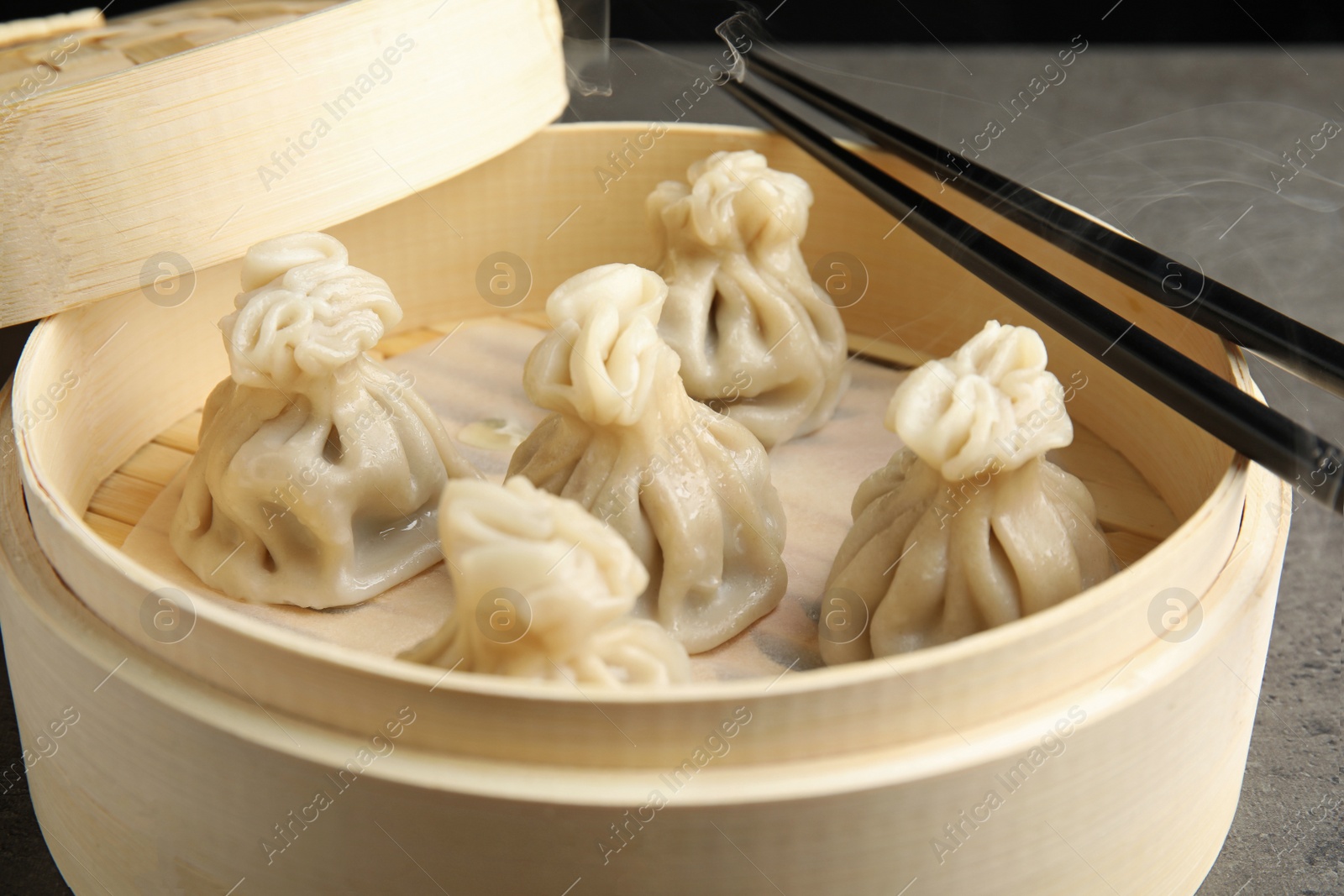 Photo of Bamboo steamer with tasty baozi dumplings and chopsticks, closeup