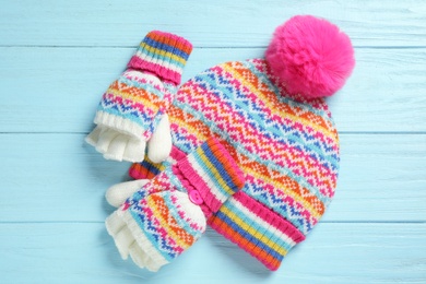 Warm knitted hat and mittens on blue wooden background, flat lay