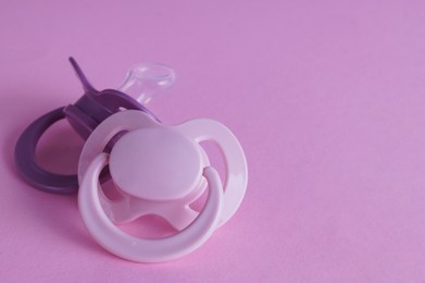 New baby pacifiers on pink background, space for text