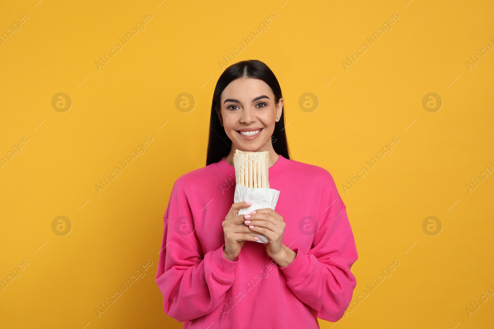 Photo of Happy young woman with delicious shawarma on yellow background