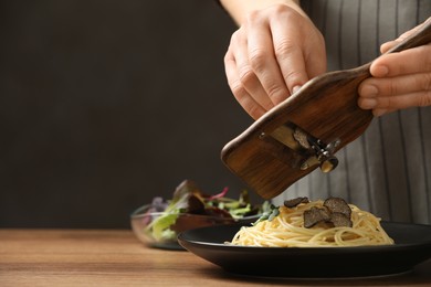 Photo of Woman slicing truffle onto spaghetti at wooden table, closeup